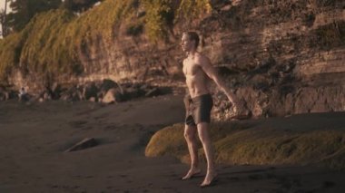 Beautiful perfect body Caucasian man does squats and jumps out outdoor.