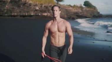 Spor yaptıktan sonra deniz kıyısında üstsüz yürüyen beyaz bir adam..