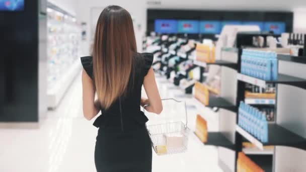 Back view of young Caucasian woman walks in cosmetics store. — Stock Video