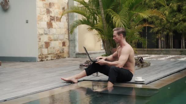 Sportlicher kaukasischer Oben-ohne-Mann arbeitet im Urlaub im Freien am Pool mit Laptop. — Stockvideo