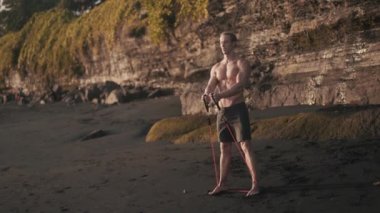 Genç atletik adam kumlu sahilde pazılarını ve trisepslerini çalıştırıyor..