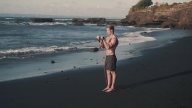 Mükemmel vücut sporcusunun yan görünüşü elastik bantla kolları eğitiyor..