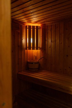 Sıcak ışıkla aydınlatılmış geleneksel ahşap bir saunanın içi. Tahta banklar, kova ve kepçe rahatlık, spa ve sağlık inzivaları için tipik bir rahatlatıcı ve rahat bir atmosfer yaratır. Rahatlama ve ısı ile ilgili konular için mükemmel illüstrasyon