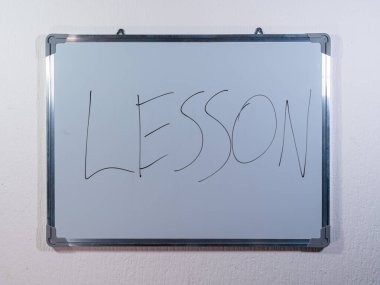 Eğitim, öğrenme ve öğretim sürecini temsil eden temiz beyaz duvar arkaplanı hakkında LESSON kavramını gösteren beyaz tahta