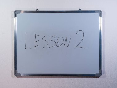Eğitim, öğrenme ve öğretim sürecini temsil eden temiz beyaz duvar arkaplanı hakkında LESSON kavramını gösteren beyaz tahta