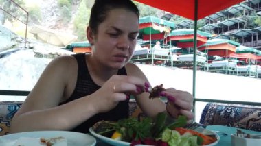 Bir kız, nehir kıyısındaki küçük bir şelalede restoranda yemek yiyor.