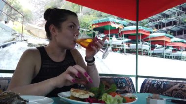 Bir kız, nehir kıyısındaki küçük bir şelalede restoranda yemek yiyor.