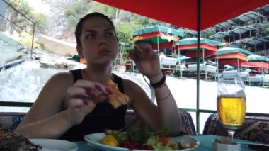 Bir kız, nehir kıyısındaki küçük bir şelalede restoranda yemek yiyor.