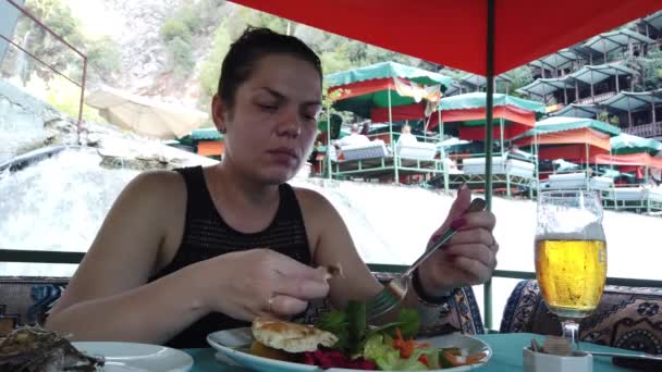山の川の上の小さな滝で水の上のレストランで食事をする女の子 — ストック動画
