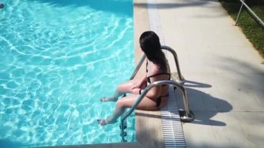Mavi su havuzunda mayo giymiş genç bir kız. Kız tatil köyünün havuzunda yüzüyor ve dinleniyor. 4K video seyahat kavramı
