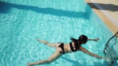 Mavi su havuzunda mayo giymiş genç bir kız. Kız tatil köyünün havuzunda yüzüyor ve dinleniyor. 4K video seyahat kavramı