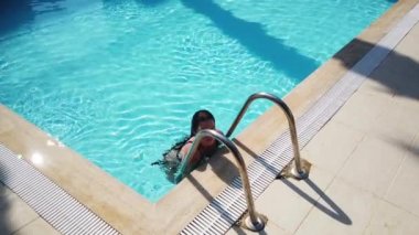Mavi su havuzunda mayo giymiş genç bir kız. Kız tatil köyünün havuzunda yüzüyor ve dinleniyor. 4K video seyahat kavramı