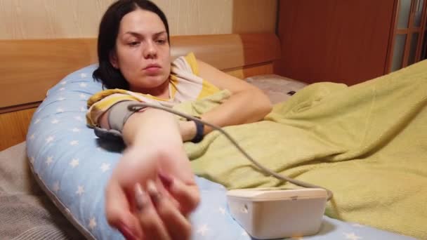 Menina em casa na cama mede a pressão com um tonômetro — Vídeo de Stock