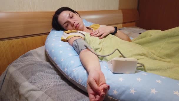 Dívka doma v posteli měří tlak s tonometrem — Stock video