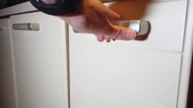 Adam mutfak dolabında bir çekmece açıyor.