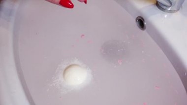 Bomba banyosu tuzu suda çözülür ve köpük oluşturur. Bir kız elinde bir banyo bombası tutuyor..