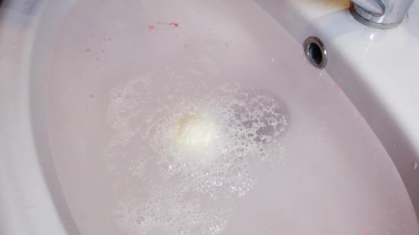 Il sale di bagno di bomba si dissolve in acqua e crea la schiuma. Una ragazza tiene in mano una bomba da bagno. — Video Stock