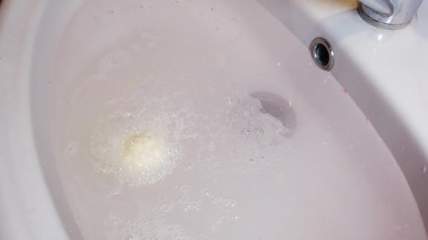 Бомбова ванна сіль розчиняється у воді і утворює піну. Дівчина тримає бомбу для ванни в руках . — стокове відео