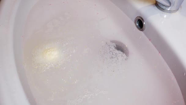 Соль для ванн-бомб растворяется в воде и образует пену. Девушка держит в руках бомбу для ванны. — стоковое видео