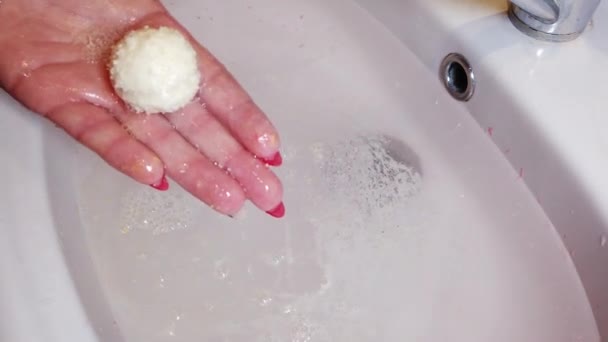 Бомбова ванна сіль розчиняється у воді і утворює піну. Дівчина тримає бомбу для ванни в руках . — стокове відео