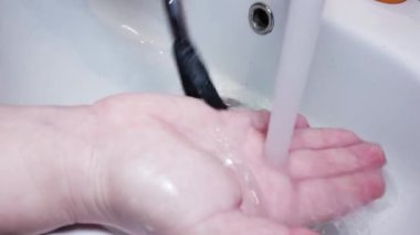 Kapalı kadın makyaj fırçalarını musluk suyuyla yıkıyor.