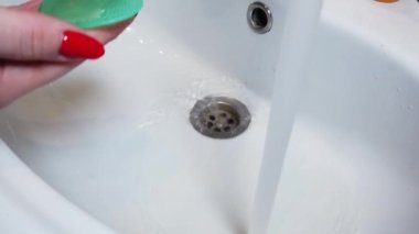 Kapalı kadın makyaj fırçalarını musluk suyuyla yıkıyor.