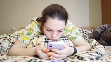 Nazik kadın yatakta uzanıyor ve akıllı telefondan mesaj yazıyor..