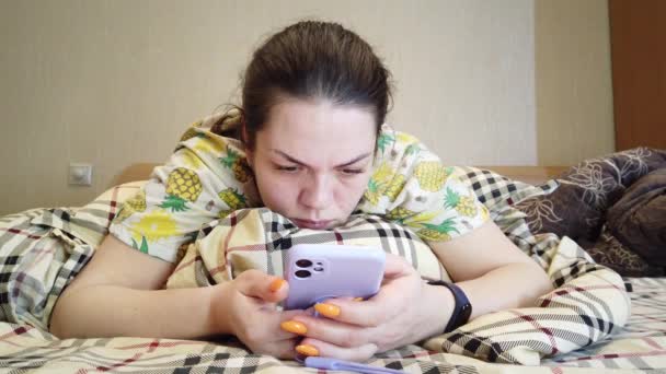 Zachte vrouw die op bed ligt en een bericht typt op de smartphone. — Stockvideo