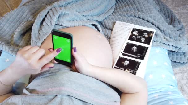 Een Zwangere Vrouw Ligt Bed Met Een Telefoon Haar Hand — Stockvideo