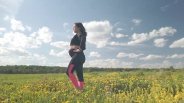 Çiçek açan bir alanda hamile bir kız spor yapıyor.