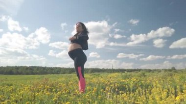 Çiçek açan bir alanda hamile bir kız spor yapıyor.