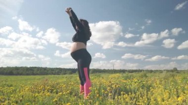 Çiçek açan bir alanda hamile bir kız spor yapıyor.