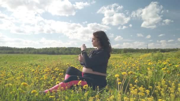 Una chica embarazada está descansando en un campo con hermosas flores amarillas — Vídeos de Stock