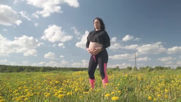 En gravid flicka vilar i ett fält med vackra gula blommor — Stockvideo