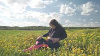 Hamile bir kız güzel sarı çiçeklerle bir tarlada dinleniyor.