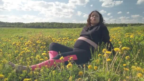 Uma menina grávida está descansando em um campo com belas flores amarelas — Vídeo de Stock