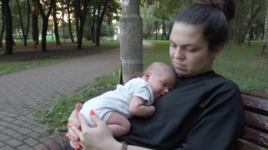Yeni doğmuş bir bebek parkta bir bankta oturan bir annenin göğsünde yatıyor.