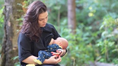 Kadın ormanda dinlenirken bebeğini emziriyor..