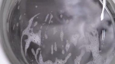 Beyaz çamaşır makinesi kirli ayakkabıları yıkar. Ev yapımı çamaşır makinesinde ayakkabı yıkamak. Cam kapıda çamaşır tozu köpüğü var..