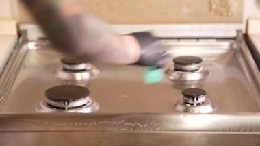 Mutfakta bir adam gaz sobasını yıkar, özel temizlik malzemelerinin yardımıyla eldiven giyer ve sünger gaz pişirme fırınının yüzeyindeki kiri temizler..