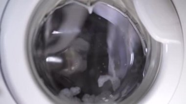 Beyaz çamaşır makinesi kirli ayakkabıları yıkar. Ev yapımı çamaşır makinesinde ayakkabı yıkamak. Cam kapıda çamaşır tozu köpüğü var..