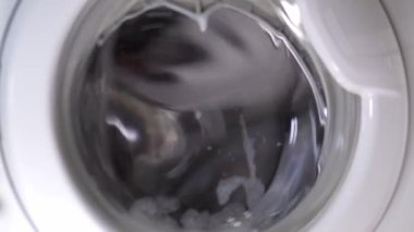 Beyaz çamaşır makinesi kirli ayakkabıları yıkar. Ev yapımı çamaşır makinesinde ayakkabı yıkamak. Cam kapıda çamaşır tozu köpüğü var..