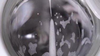 Beyaz çamaşır makinesi kirli ayakkabıları yıkar. Ev yapımı çamaşır makinesinde ayakkabı yıkamak. Cam kapıda çamaşır tozu köpüğü var..