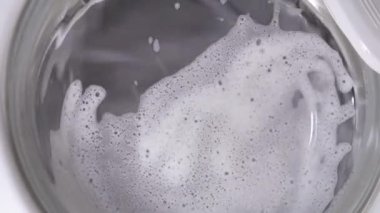 Beyaz çamaşır makinesi kirli ayakkabıları yıkar. Ev yapımı çamaşır makinesinde ayakkabı yıkamak. Cam kapıda çamaşır tozu köpüğü var..