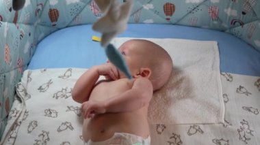 Bebek arabası ve yeni doğmuş bir bebeğin beşiğinde farklı oyuncaklar asılı. Yeni doğmuş erkek bebek beşiğinde yatar ve bebek arabasında asılı durur..