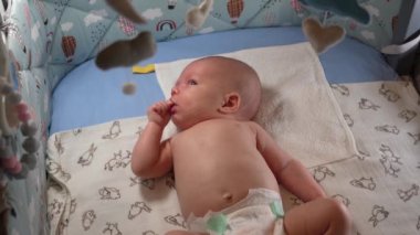 Bebek arabası ve yeni doğmuş bir bebeğin beşiğinde farklı oyuncaklar asılı. Yeni doğmuş erkek bebek beşiğinde yatar ve bebek arabasında asılı durur..