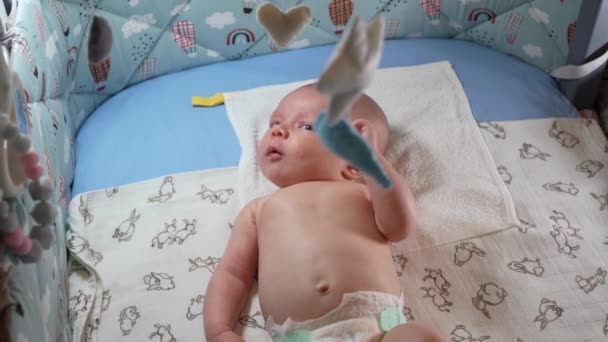 婴儿车 不同的玩具挂在新生儿的婴儿床上 新生男婴躺在婴儿床里 看着挂在床上的婴儿手机 — 图库视频影像