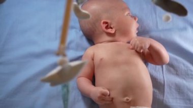 Çocuk, bebek beşiğinin üzerinde dönen el yapımı yumuşak oyuncaklarla müzikal bebek hareketine bakıyor..