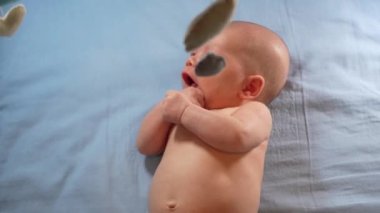Çocuk, bebek beşiğinin üzerinde dönen el yapımı yumuşak oyuncaklarla müzikal bebek hareketine bakıyor..