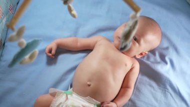 Çocuk, bebek beşiğinin üzerinde dönen el yapımı yumuşak oyuncaklarla müzikal bebek hareketine bakıyor..